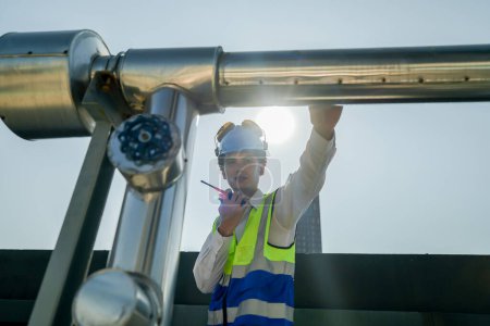 Urban rooftop scene showing a young engineer with a radio, inspecting and adjusting equipment in a sunny city environment. Safety and precision at work.