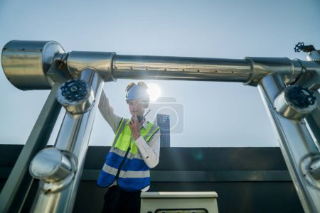 Photo for Urban rooftop scene showing a young engineer with a radio, inspecting and adjusting equipment in a sunny city environment. Safety and precision at work. - Royalty Free Image