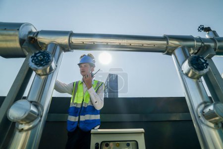 Photo for Engineer in safety gear conducts inspection on large industrial water tanks on a building rooftop. Professional engineer meticulously checks connectivity and status of piping on an urban rooftop. - Royalty Free Image
