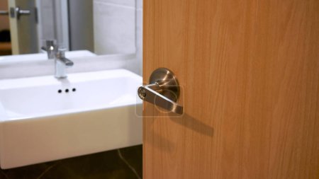 Photo for Bathroom door handles,door with stainless knob door half open in front of interior bathroom white sink of washing hands and mirror - Royalty Free Image