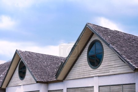 Téléchargez les photos : Belle maison en bois toit avec une fenêtre ronde sur fond bleu ciel - en image libre de droit