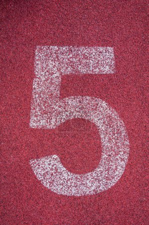 Foto de Número cinco en el hipódromo. Número de pista blanca en pista de carreras de goma roja, textura de pistas de carreras en estadio - Imagen libre de derechos
