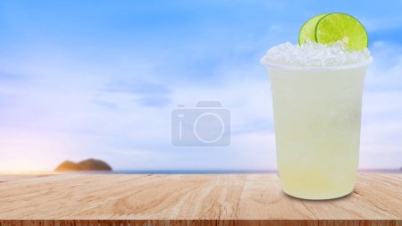 Photo for Cool freshly made lemonade in a plastic cups with crushed ice and lemon slices on wooden table with beach landscape nature background - Royalty Free Image