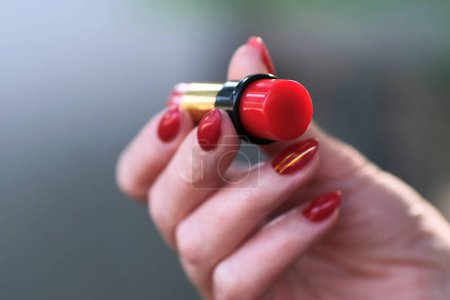 Foto de Lápiz labial rojo en mano femenina con manicura roja, mano con lápiz labial. - Imagen libre de derechos