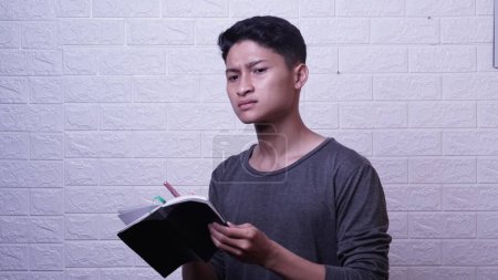 Téléchargez les photos : Asiatique homme en chemise grise tenant livre et stylo - en image libre de droit