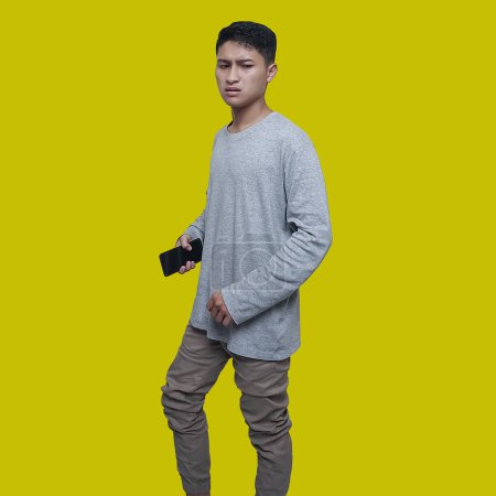 Junger Asiate hält ein Handy in der Hand, während er aufgebracht denkt