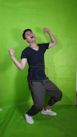 Un joven asiático guapo con una expresión feliz hasta que sus manos están arriba con un grito verde
