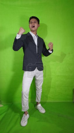 Photo for A handsome Asian young man with a happy expression until his hands are up with a green screan - Royalty Free Image