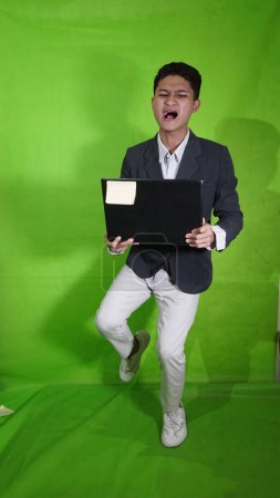 Der gut aussehende asiatische junge Mann trug einen Laptop mit einem fröhlichen Gesichtsausdruck, als wollte er fliegen und fallen