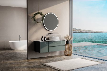 modernes Badezimmer mit Wänden in Beige- und Erdtönen, weißer Badewanne, grünem Waschtisch, schwarzem Spiegel, Waschbecken, Terrazzoboden und Blick aus dem Fenster auf Pool und Meer