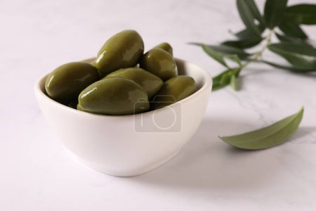 Foto de Tazón con sabrosas aceitunas y hojas verdes en la mesa - Imagen libre de derechos