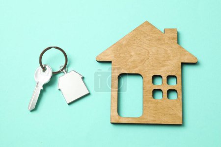 Metallic key with keychain and wooden house on color background