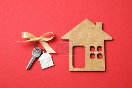 Metallic key with keychain and wooden house on color background