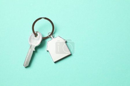 Metallic key with keychain in shape of house on color background