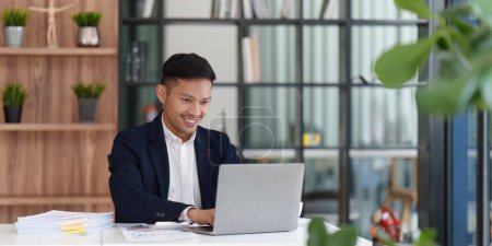Smiling Asian Banker makes financial report and studies annual figures, analyzes profits. Accountant checks status of financial.