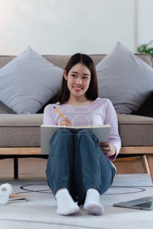 Online education, e-learning. Asian woman in stylish casual clothes, studying using a laptop, listening to online lecture, taking notes, online study at home. Poster 655989652