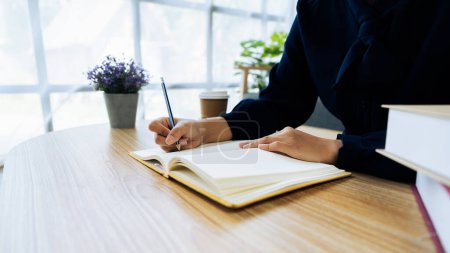 Photo for Close up young woman sit at table hold pencil take notes to paper notebook working studying. Female student businesswoman employee write records to daily planner by hand at home work desk. - Royalty Free Image
