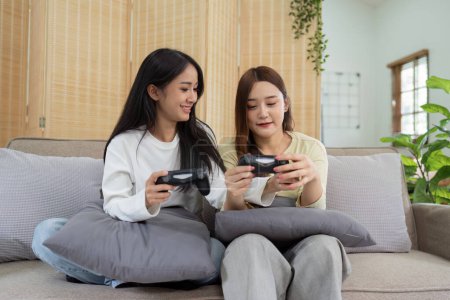 Photo for Asian beautiful lesbian gay couple enjoy play game together in Livingroom. Two female friend sit on sofa in living room, feel happy to play joystick game at home.. - Royalty Free Image