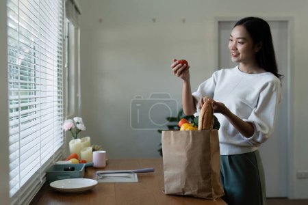 Lieferung biologischer Lebensmittel. Glückliche junge Frau packt Tasche mit frischem Gemüse in Küche aus.