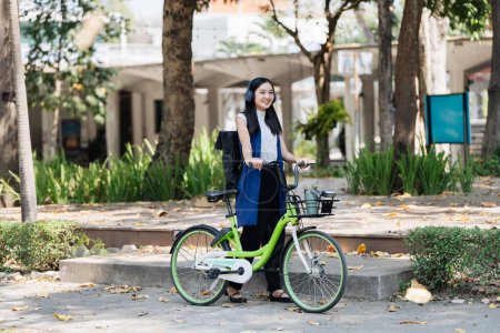Asiatische junge Geschäftsfrau radelt für umweltfreundliche grüne Energie zur Arbeit und hört Musik mit Kopfhörer, während sie in der Stadt pendelt. Umweltfreundlich.