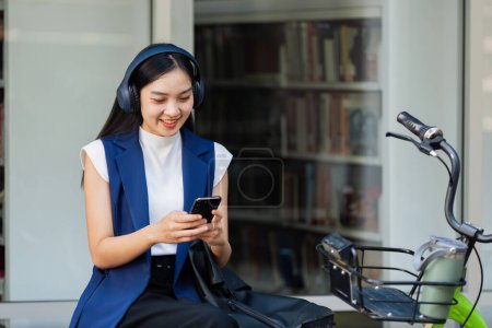 Asiatische junge Geschäftsfrau radelt mit umweltfreundlicher grüner Energie zur Arbeit und nutzt das Smartphone, während sie in der Stadt pendelt. Umweltfreundlich.