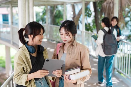 Asiatische Studenten unterhalten sich mit Tablet und Büchern auf dem Campus-Laufsteg. Hochschulkonzept.