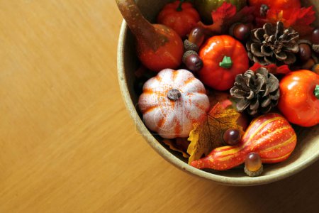 Photo for An arrangement of of plastic pumpkins, acorns, pinecones, and autumnal fabric leaves, in a ceramic bowl, set on a wooden table top - Royalty Free Image