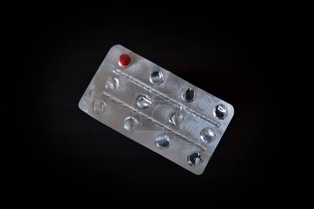 Photo for One red pill remains in a used medicine tablet blister pack. Shot isolated above a dark wood effect background. - Royalty Free Image