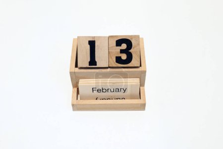 Primer plano de un calendario perpetuo de madera que muestra el 13 de febrero. Disparo de cerca aislado sobre un fondo blanco 