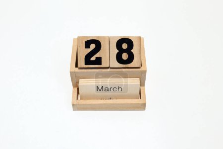 Primer plano de un calendario perpetuo de madera que muestra el 28 de marzo. Disparo de cerca aislado sobre un fondo blanco