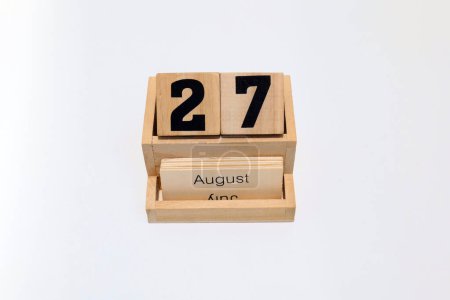 Gros plan d'un calendrier perpétuel en bois montrant le 27 août. Plan rapproché isolé sur fond blanc