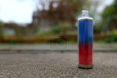 Vape macro with shallow depth of field. The vape is standing on end on a concrete path.