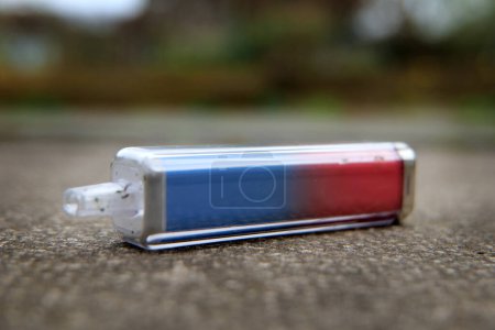 Discarded electronic cigarette vape macro with shallow depth of field. The vape has been left lying on a concrete path