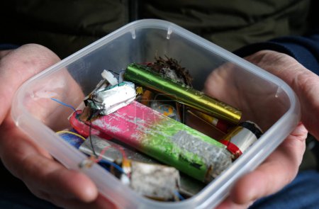 White male holding clear plastic tub containing a selection of discarded electronic cigarette vapes.