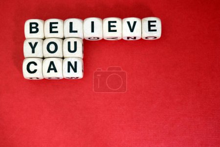 Believe You Can positive Mantra buchstabiert mit hölzernen Wortwürfeln, gesetzt über einem roten Papphintergrund.