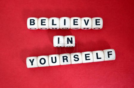 Croyez en vous-même mantra positif épeautre en utilisant des dés de mot en bois au-dessus d'un fond de carton rouge vibrant.