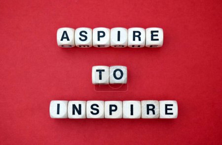 Aspire to Inspire positive Mantra buchstabiert mit hölzernen Wortwürfeln über einem lebendigen roten Papphintergrund.