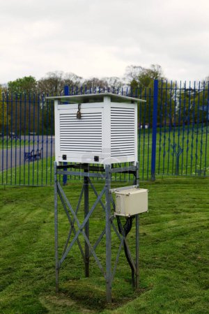 Una caja de grabación meteorológica blanca de Stevenson Screen colocada en un marco de metal en un parque público.