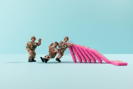 Photo for Toy soldiers stoping domino effect of pink domino on cyan - Royalty Free Image