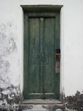 An ancient green wooden door on the old white wall, part of the synagogue.