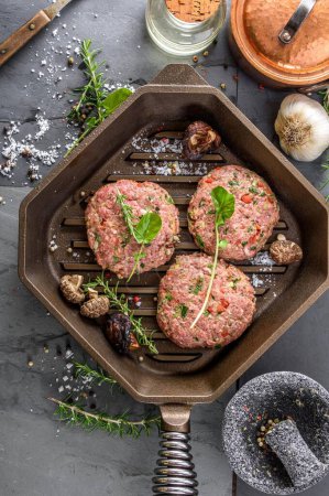 Téléchargez les photos : Création gastronomique : Vue du dessus des galettes de hamburger crues avec des épices Étourdissant dans une casserole en fonte, en attendant la perfection culinaire en résolution 4K - en image libre de droit