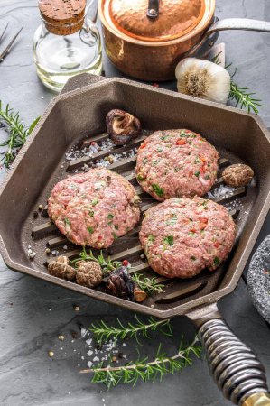 Foto de Creación gourmet: Vista superior de las hamburguesas crudas con especias Sizzling en una sartén de hierro fundido, esperando la perfección culinaria en resolución 4K - Imagen libre de derechos
