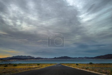 Desert Serenity: 4K Ultra-HD-Bild der Wüstenstraße, die zum Seeufer mit Wolken bei Sonnenuntergang führt