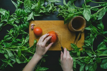 Farm-to-Table Cooking: Woman Slicing Tomato on Cutting Board Surrounded by Fresh Green Leaves in 4K image