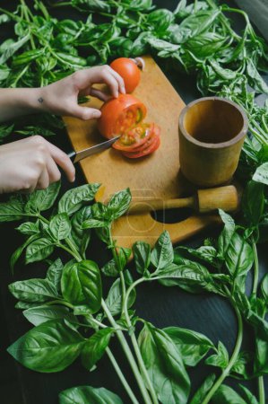 Farm-to-Table Cooking: Woman Slicing Tomato on Cutting Board Surrounded by Fresh Green Leaves in 4K image