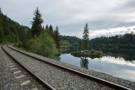 Atemberaubendes 4K-Bild: Ruhige Szene von Bahngleisen, die zum See und zur bewaldeten Insel führen