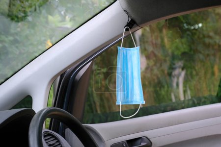 Photo for A medical protective mask hangs on the car mirror to protect against bacteria and viruses while driving. Pandemic - Royalty Free Image