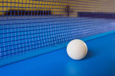 Foto de Pelota de tenis de mesa blanca sobre mesa azul con red. Tenis de mesa. - Imagen libre de derechos