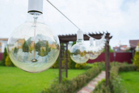 Foto de Un primer plano de una lámpara incandescente colgando en el patio trasero del jardín. - Imagen libre de derechos