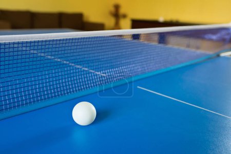 Foto de Una pelota blanca de tenis para Ping-Pong en una mesa azul. Un juego de ping-pong. Juegos de deporte. - Imagen libre de derechos